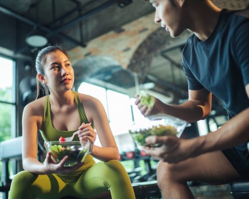 Asian man and woman eating salad for health together. Two Asian people healthy eating salad after exercise at fitness gym. Healthy lifestyle.